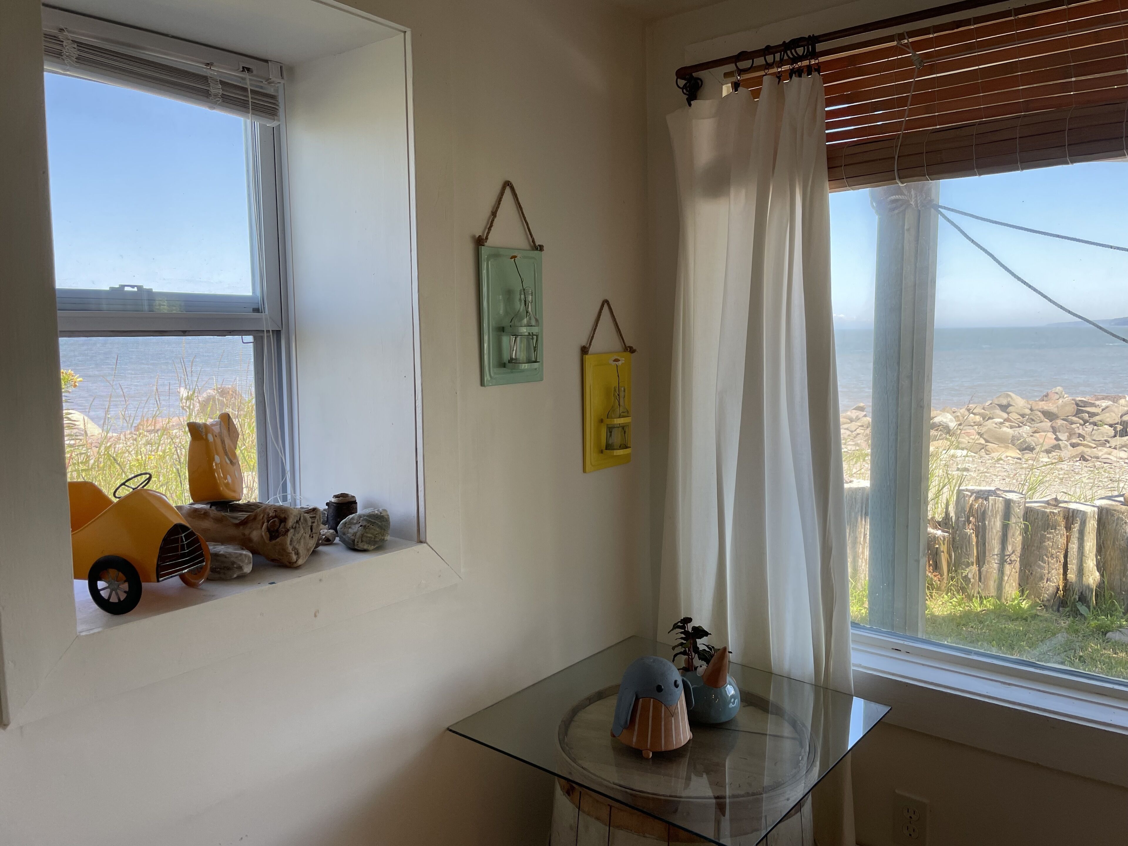 A room with a window overlooking a rocky beach, a small table with decorative items, and a toy car on the windowsill.