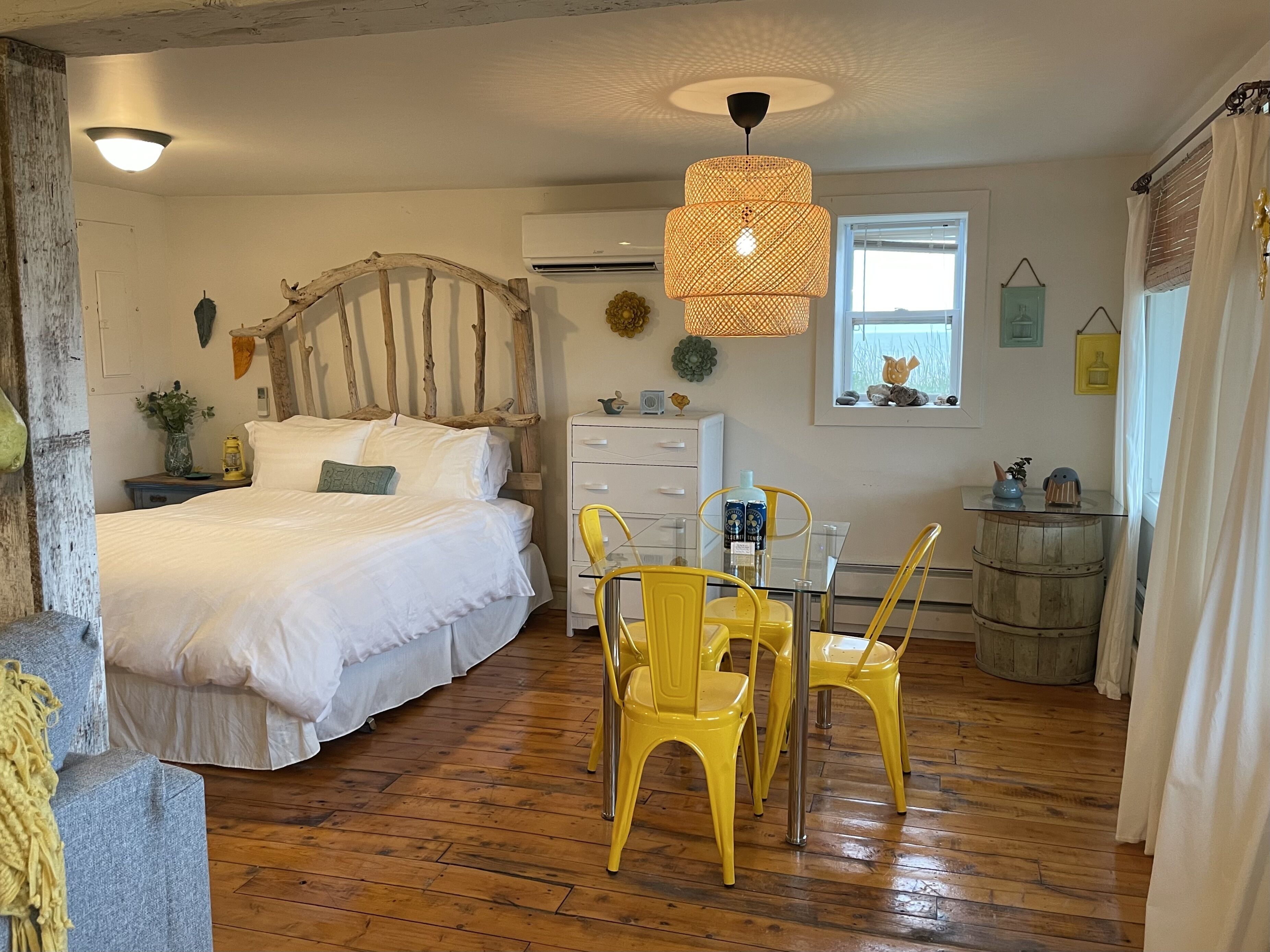 A bedroom with a bed, a dresser, a chair, a table, and a hanging light fixture.