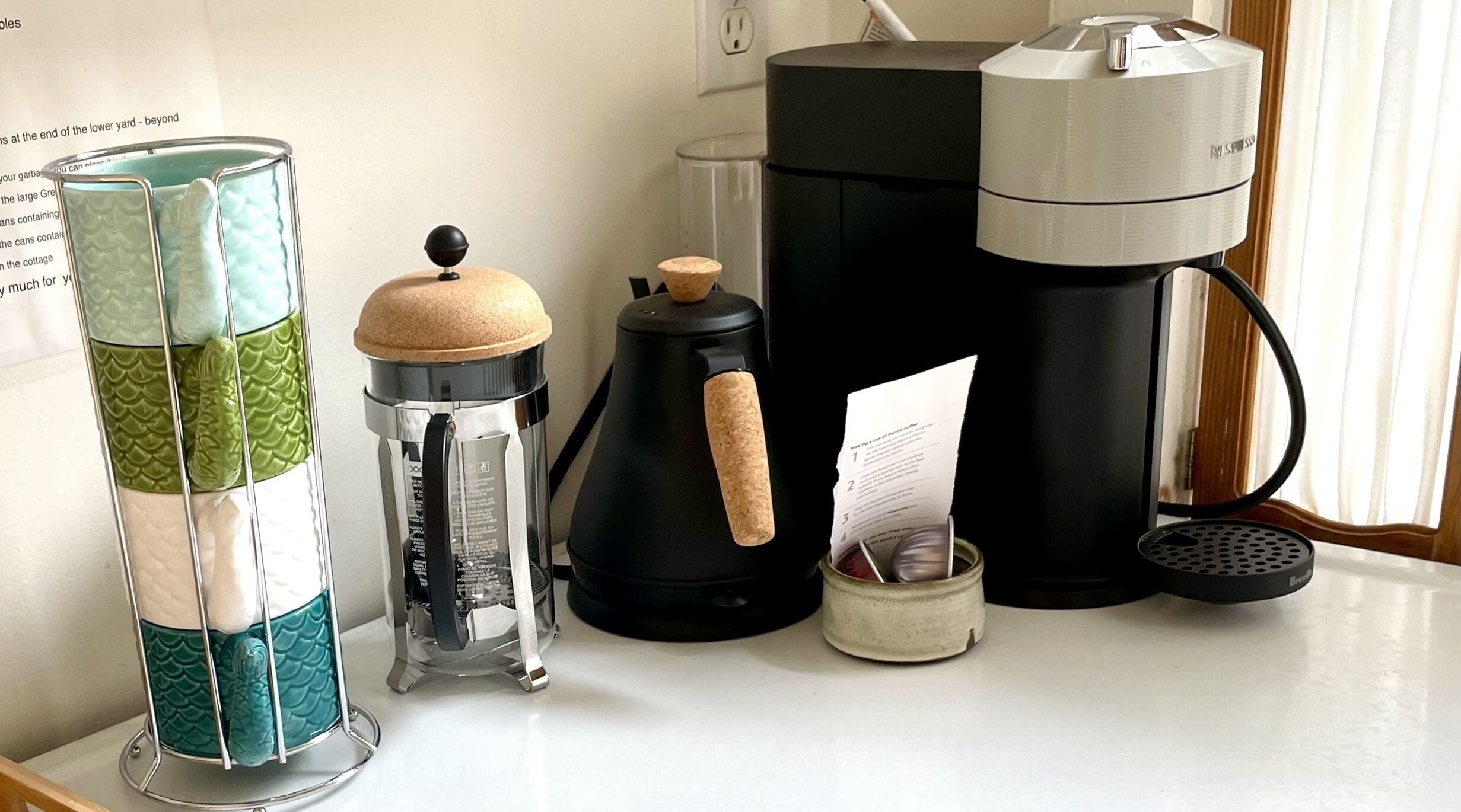 A kitchen counter with a coffee maker, a French press, a sifter, and a container with a lid.