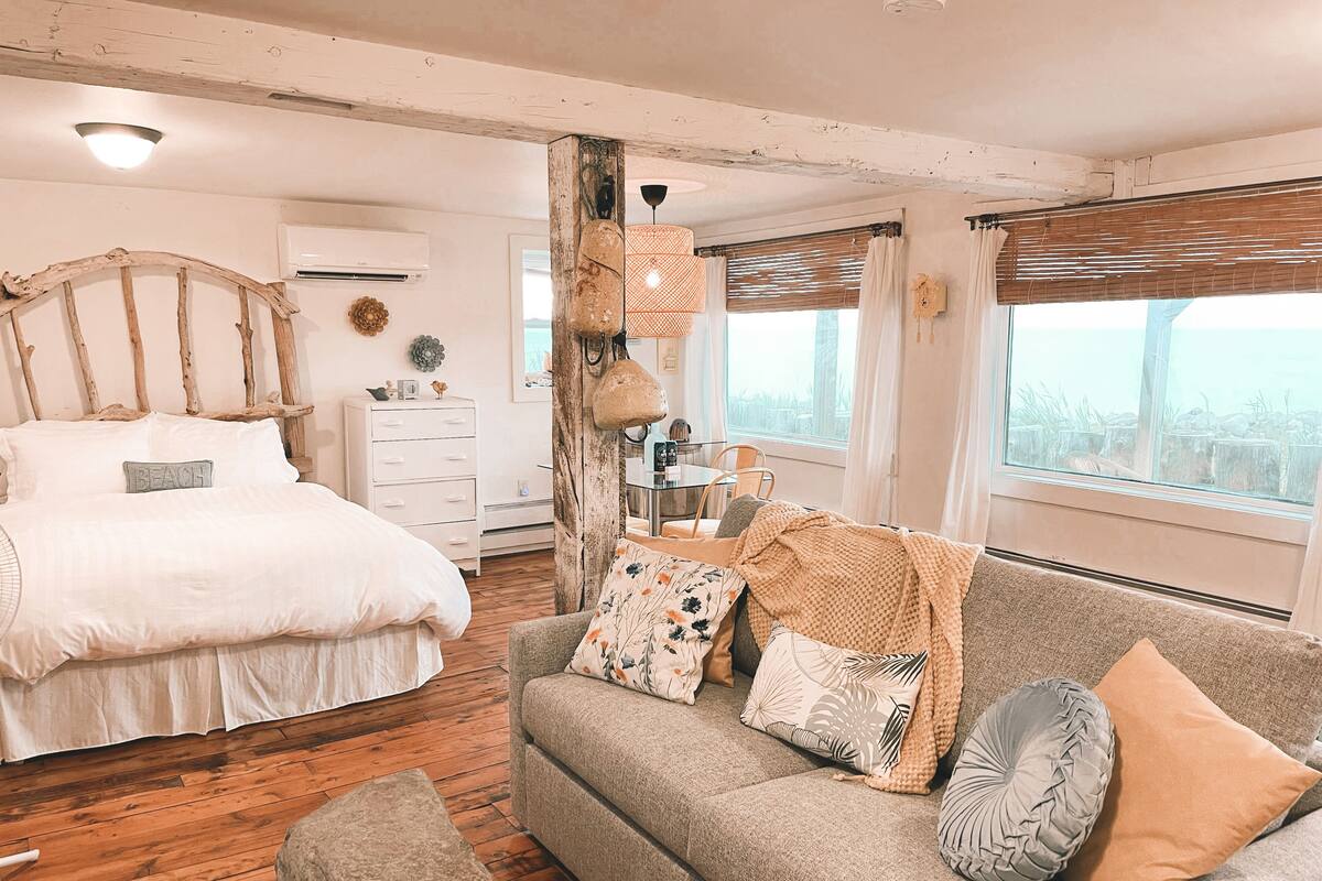 Ein Schlafzimmer mit einem Bett, einer Couch, Holzboden und einem Vorhangfenster.