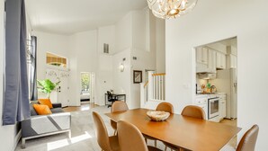 Ein moderner Essbereich mit einem Holztisch und braunen Stühlen, einer Couch mit orangefarbenen Kissen sowie einer Treppe zu einer Küchenzeile.