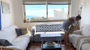 A living room with a sofa, a coffee table with a bowl and books, a window with blinds, and a view of the sea. - Holiday home with beautiful sea views, 3 minutes walk from the beach (Località Timpi Russi)