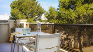 A balcony with a table and chairs, a glass of water, and a view of trees and buildings. - 5 min to Cala Crancs | Terrace & Pool (Salou)