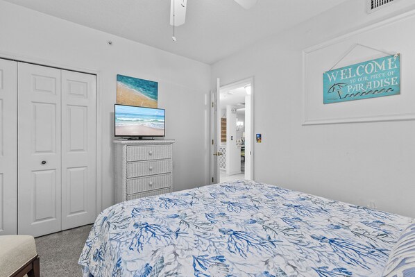 Une chambre à coucher comprenant un lit, une télévision, une commode et une porte donnant sur une autre pièce.