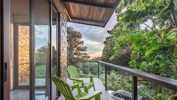 A balcony with two green chairs, a car, and a view of trees and a cloudy sky.