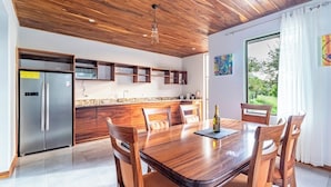 A modern kitchen with wooden cabinets, a stainless steel refrigerator, and a dining area with a wooden table and chairs.