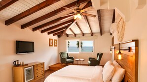 A bedroom with a wooden ceiling, a bed with white bedding, a television, a small table, two chairs, and a window with a view of the sea. - Casa Linn Boutique Hotel (Ayvacik)