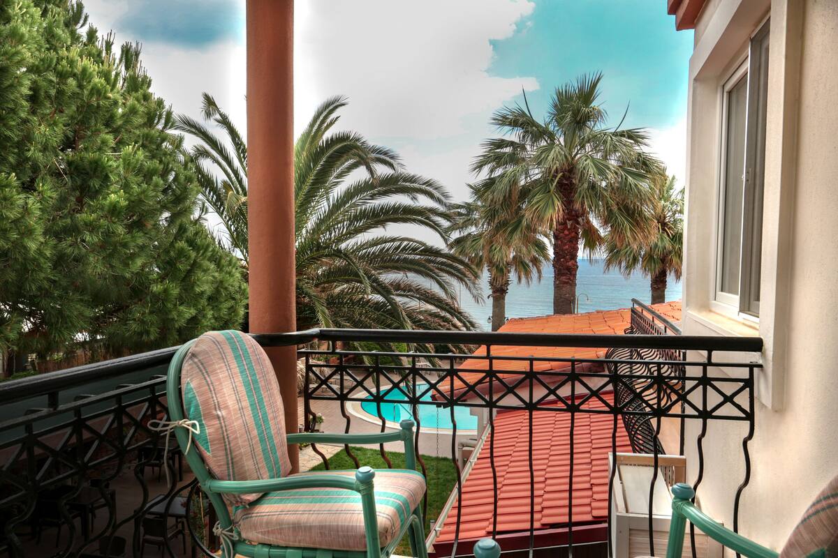 A balcony with a view of the sea, palm trees, and a pool.