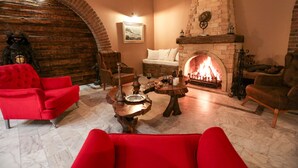 A cozy living room with a fireplace, red armchairs, a coffee table, and a stone fireplace surround. - Casa Linn Boutique Hotel (Ayvacik)