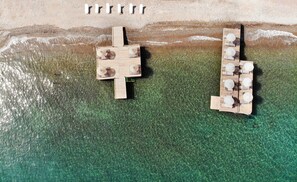 An aerial view of a beachside wooden deck with seating and umbrellas, overlooking clear turquoise water.