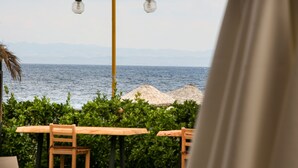 A seaside view with a wooden table and chairs, a lamp post, and a thatched umbrella. - Casa Linn Boutique Hotel (Ayvacik)