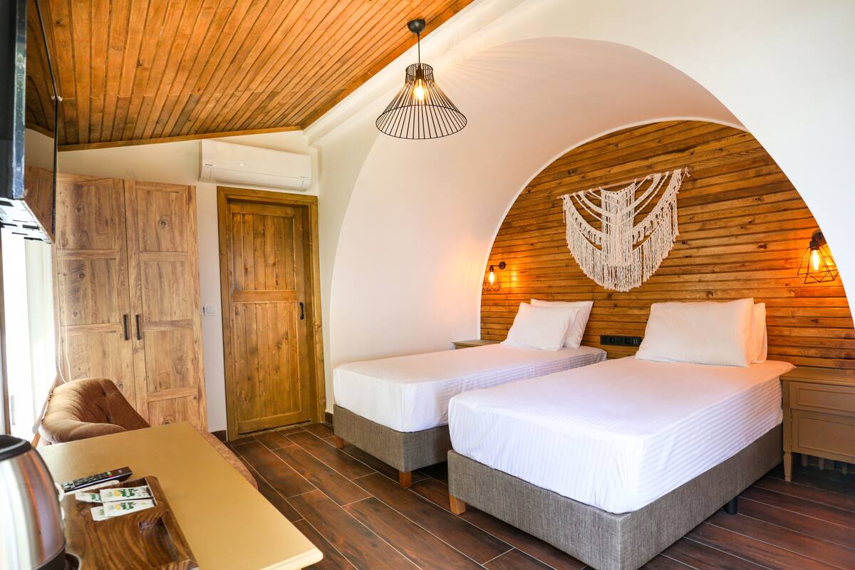 A cozy room with two beds, wooden walls, a wooden ceiling, and a hanging light fixture.