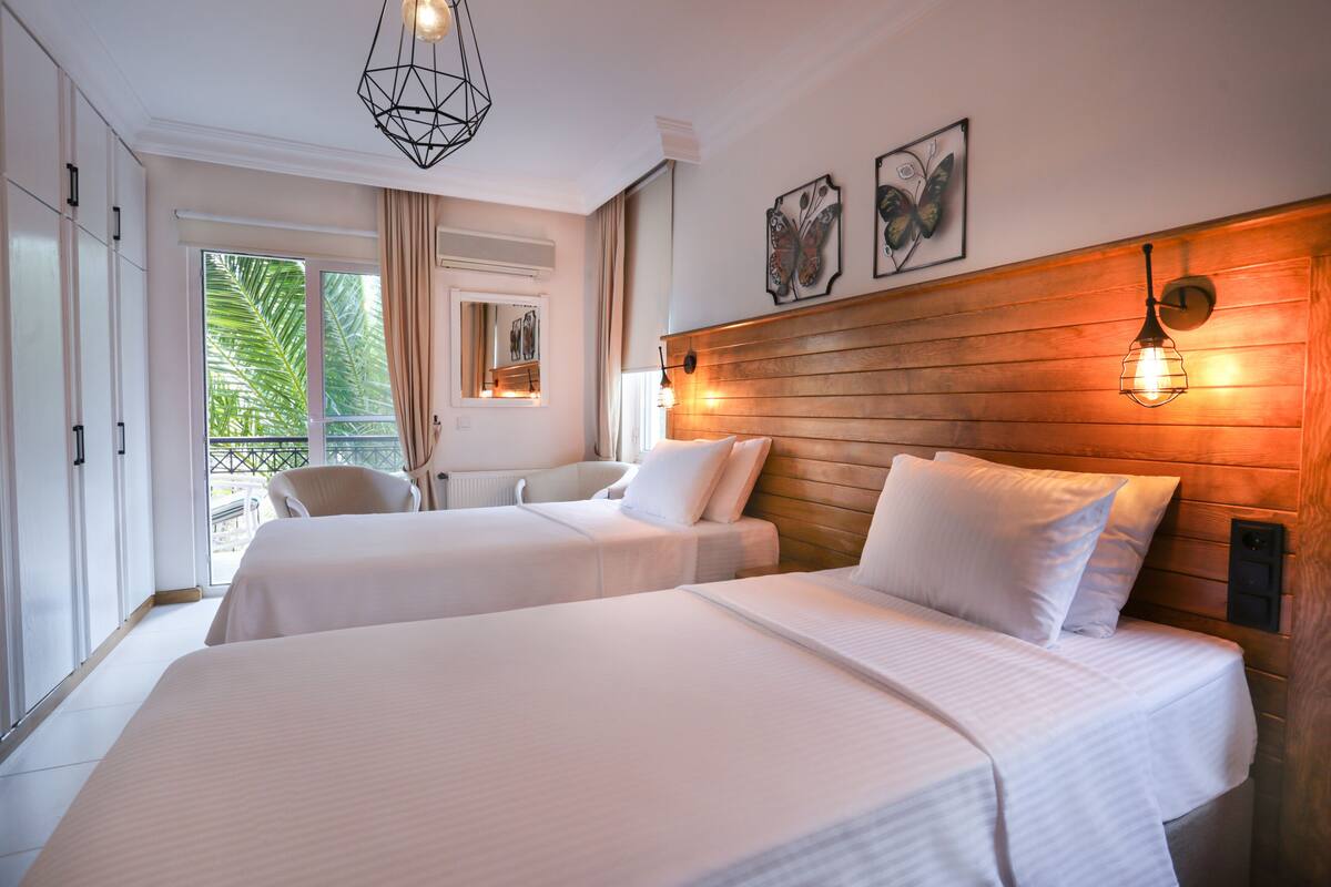 A hotel room with two beds, a wooden headboard, a balcony with a view, and a modern pendant light.