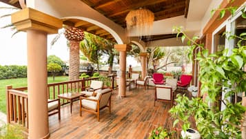 An outdoor patio with wooden furniture, a thatched ceiling, and a view of the garden.