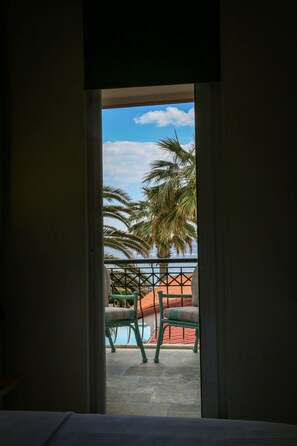 Una puerta abierta que da a un balcón con piscina, palmeras y sillas.