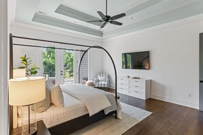 Un dormitorio con cama de dosel, ventilador de techo, ventana grande, televisor y cómoda blanca.
