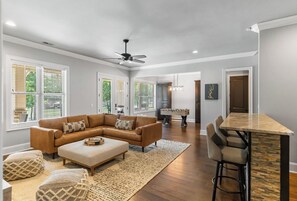 Uma sala de estar espaçosa com sofá seccional, apoio para os pés e um espaço bar com banquetas.