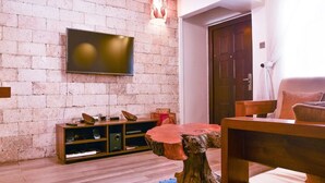 A living room with a brick wall, a flat-screen TV mounted above a wooden shelf, and a rustic wooden coffee table. - Secure, 2 bedroom house in a quiet neighborhood. (Nairobi County)