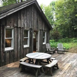 A rustic wooden cabin with a round wooden table and benches, two Adirondack chairs, and a deck. - Secure, 2 bedroom house in a quiet neighborhood. (Nairobi County)