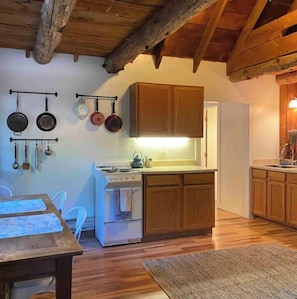 A compact kitchen with wooden cabinets, a white stove, and hanging pots.
