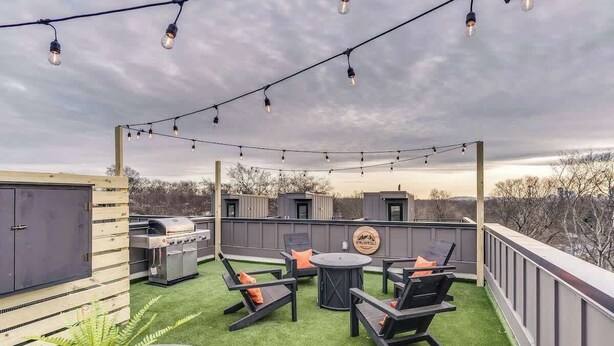 Une terrasse extérieure équipée d’un barbecue, d’un espace salon et de guirlandes lumineuses.
