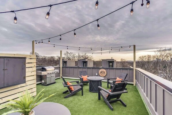 Un patio exterior con una parrilla, zona de estar y luces colgantes.
