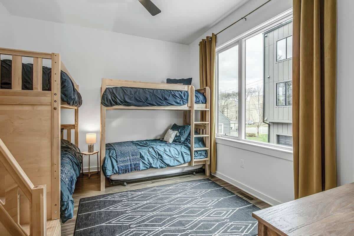 A dormitory room with bunk beds, a small table, a lamp, and a window with curtains.