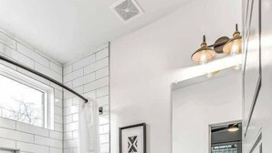 Une salle de bain moderne avec une douche carrelée de carreaux blancs, des toilettes blanches, un lavabo blanc avec un miroir et un sol à motifs en chevrons.