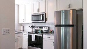 A modern kitchen with white cabinets, a stainless steel refrigerator, a microwave, and an oven. - Easy Walk to Beach, Boardwalk, & Lake! King Beds! (Carolina Beach)