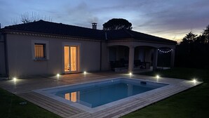 Una casa con piscina, un patio con illuminazione esterna e una zona coperta con posti a sedere.