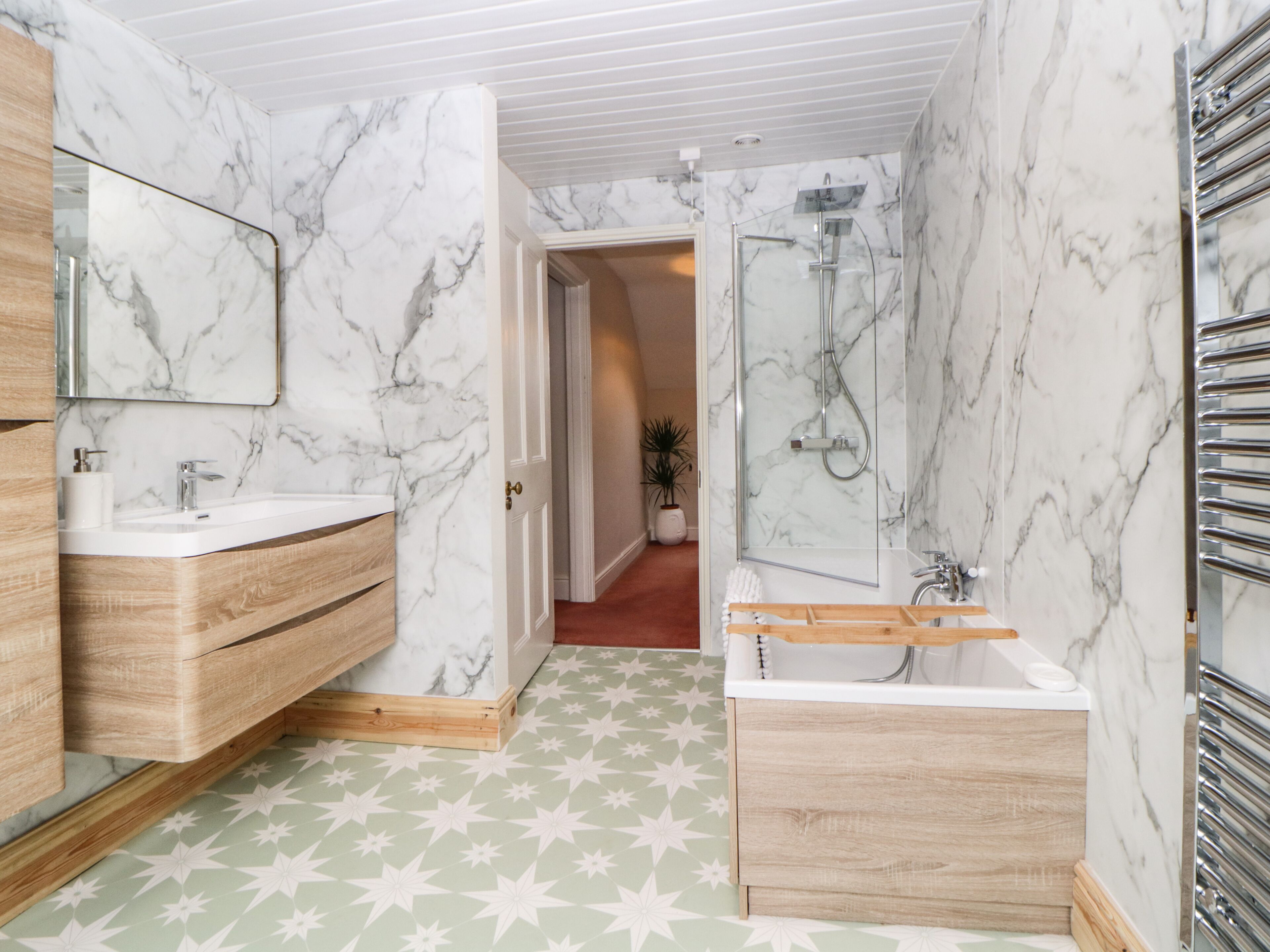 A modern bathroom with marble walls, a wooden vanity, a bathtub, and a shower area.