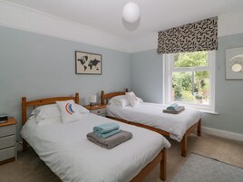 A hotel room with two single beds, a bedside table with a lamp, a world map on the wall, and a window with a view of greenery.