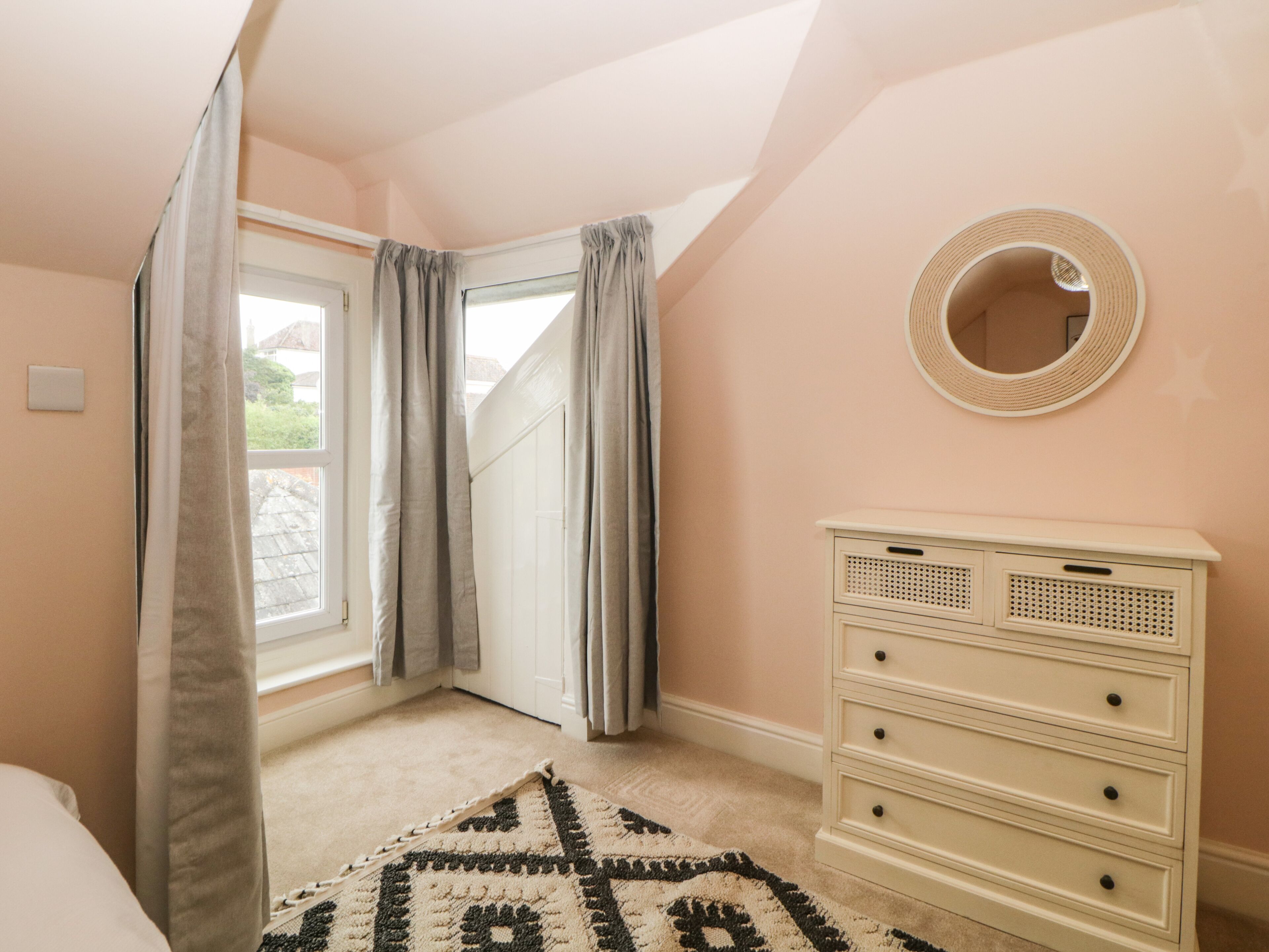 A bedroom with a large window, a dresser, and a patterned rug.