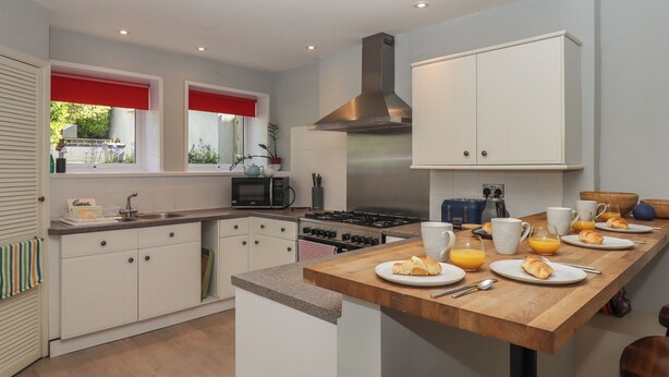 Una cocina moderna con armarios blancos, una encimera de madera y una mesa para el desayuno con cruasanes y jugo de naranja.