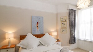 Una cama bien hecha con almohadas, dos mesitas de noche con lámparas, una pared decorada con cuadros y una ventana con cortinas.