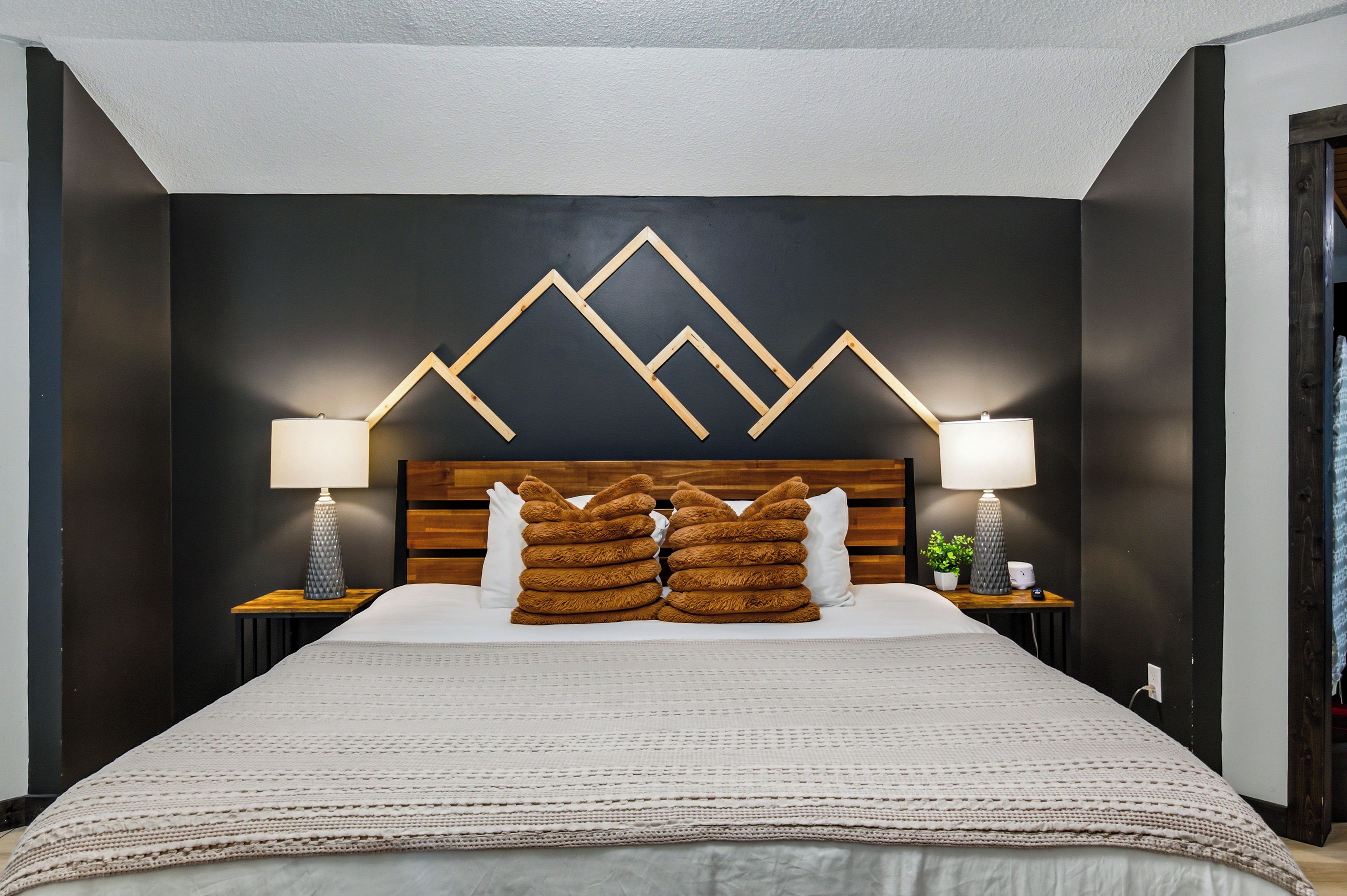 Una camera d'albergo con un letto grande, due comodini con lampade, un elemento decorativo geometrico e una testiera in legno.