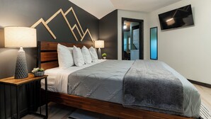 Um quarto moderno com cama de madeira, duas luminárias de cabeceira, um ornamento geométrico na parede e uma TV de tela plana fixada na parede.