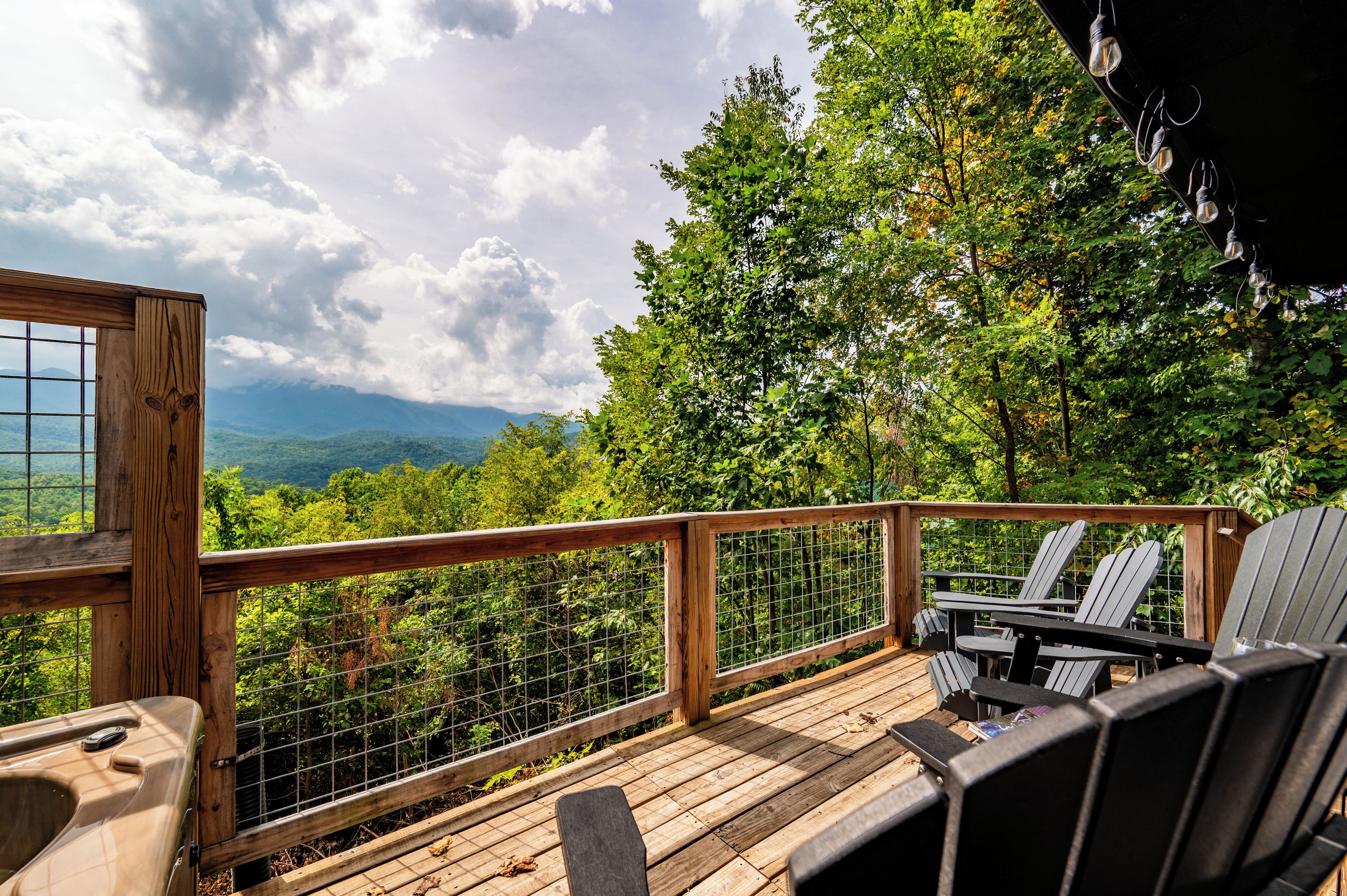 A wooden deck with a metal railing, outdoor seating, and a view of a mountainous landscape.