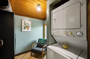 A laundry room with a vintage washer and dryer, a chair, and a framed plant on the wall.