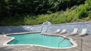 Una piscina con una cascada, rodeada de sillas de descanso y un patio de hormigón.