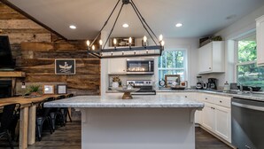 Une cuisine moderne dotée d’un îlot central, d’éléments décoratifs en bois, de meubles blancs et d’un luminaire suspendu.