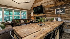Un intérieur rustique en bois, avec une grande table à manger, un canapé en cuir et un téléviseur fixé au mur.