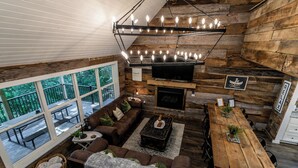 Un intérieur chaleureux de type chalet, avec un revêtement mural en bois, une cheminée, un téléviseur et un coin repas.