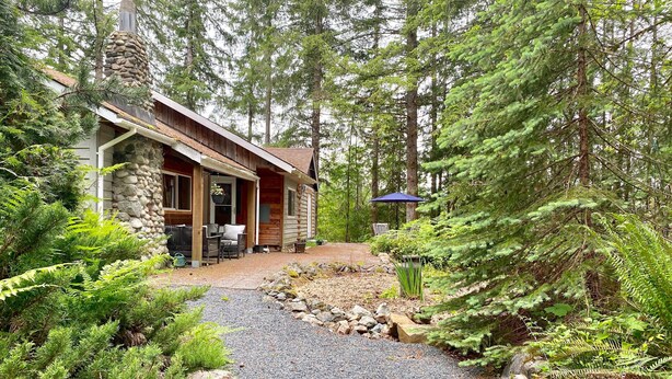 A rustic cabin with a stone chimney, wooden exterior, and a gravel path leading to a patio with outdoor furniture. - Large cabin on rural farm.  Private, relaxing, close to Stamp Falls Park. (Port Alberni)