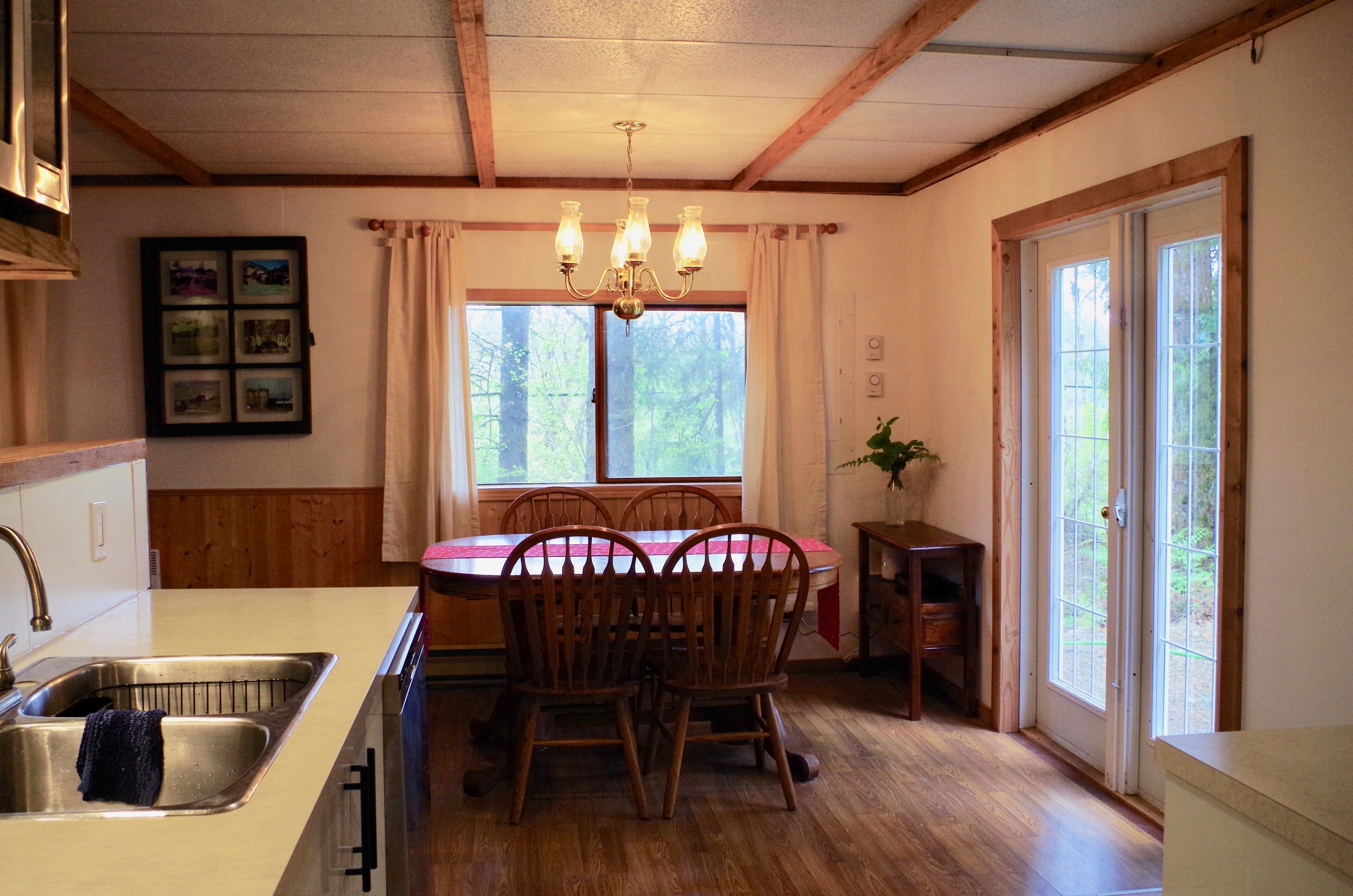 A dining area with a wooden table and chairs, a chandelier, and a window with curtains.