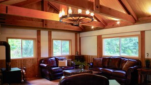 A cozy living room with leather sofas, a wooden ceiling, and large windows. - Large cabin on rural farm.  Private, relaxing, close to Stamp Falls Park. (Port Alberni)