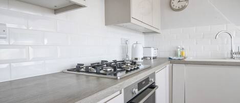 A modern kitchen with white cabinetry, a gas stove, an oven, a sink, and a clock on the wall.