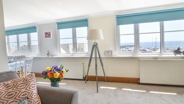 A spacious room with a high ceiling, large windows with blue blinds, a tripod lamp, a white chair, and a sofa with patterned cushions.