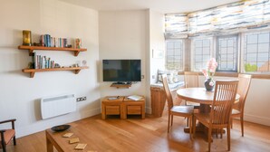 A modern living room with a flat-screen TV, wooden furniture, and a dining area with a view through large windows. - 3 Coram Tower (Lyme Regis)
