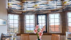 A room with a round table, wooden chairs, a vase with pink flowers, and a view of the sea through large windows with a grid pattern. - 3 Coram Tower (Lyme Regis)